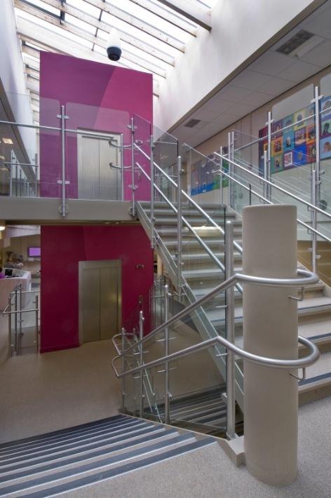 Twin height brushed stainless steel handrails returning around a concrete column on a school staircase